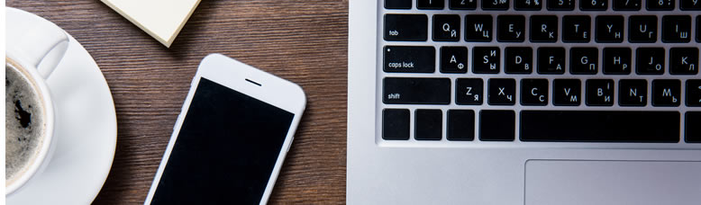 Top view of a keyboard alongside a mobile device and cup of coffee.