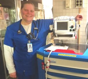 Nurse in blue scrubs, smiling next to medical equipment