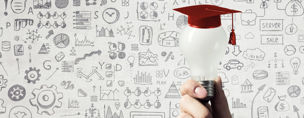 Hand holding a lightblub with a red graduation cap on top of it. Background is a white wall with doodles of gears and graphs.