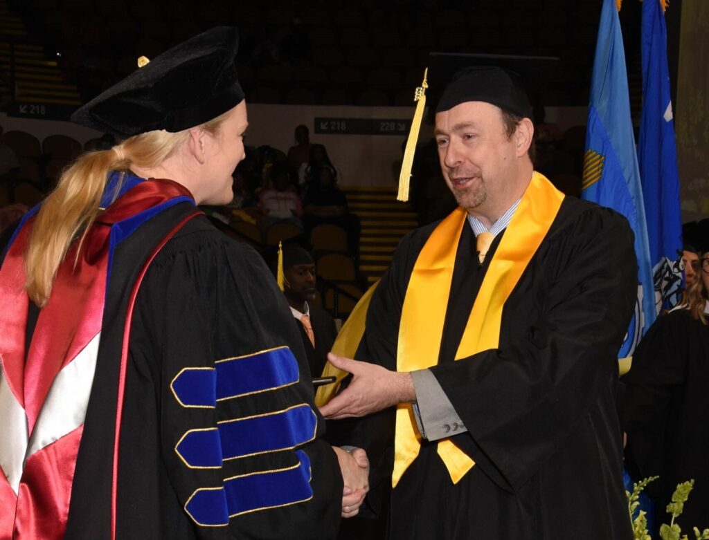Torry in a cap and gown receiving his diploma during UW-Milwaukee's commencement. 