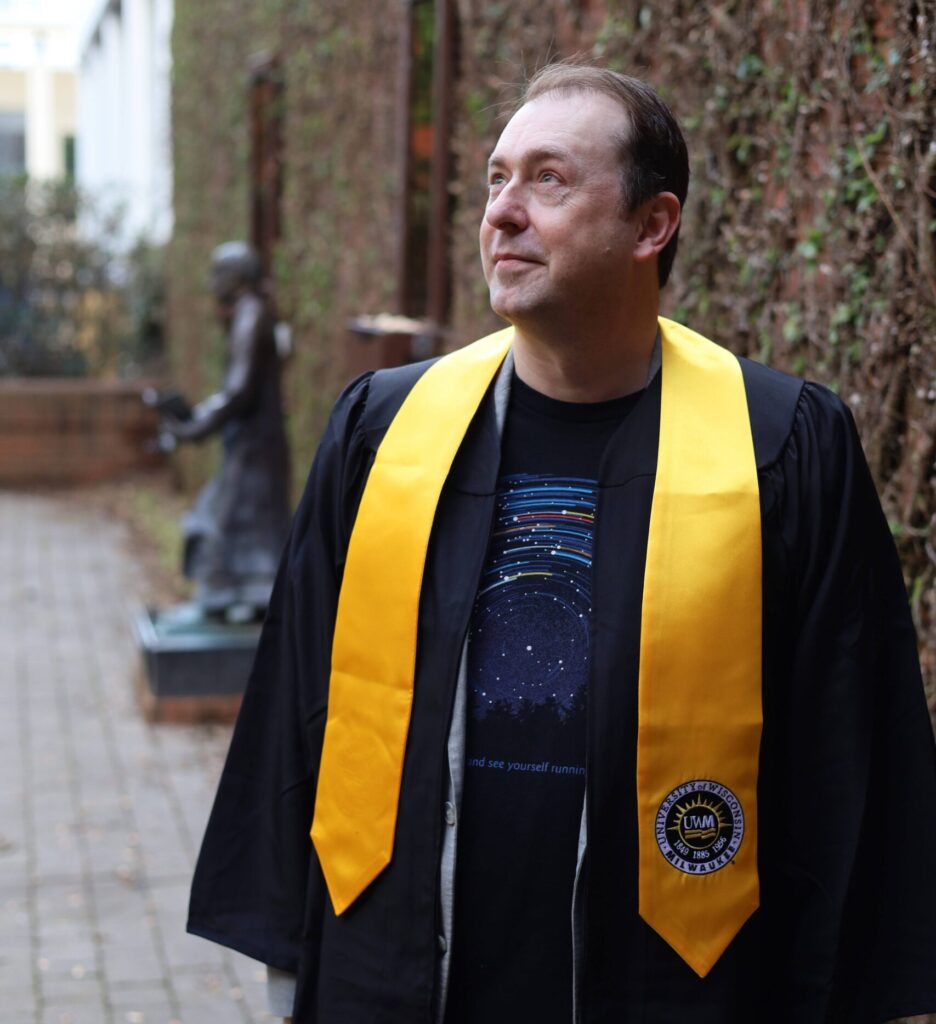 Torry wearing a cap and gown with a space-themed undershirt as he looks up at the sky. 