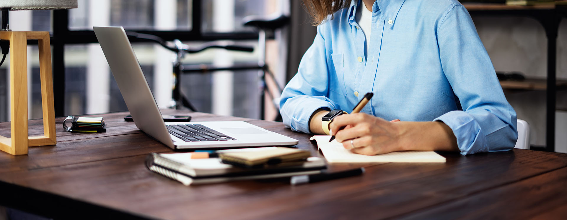 Student writing on a notebook while studying in front of a laptop.