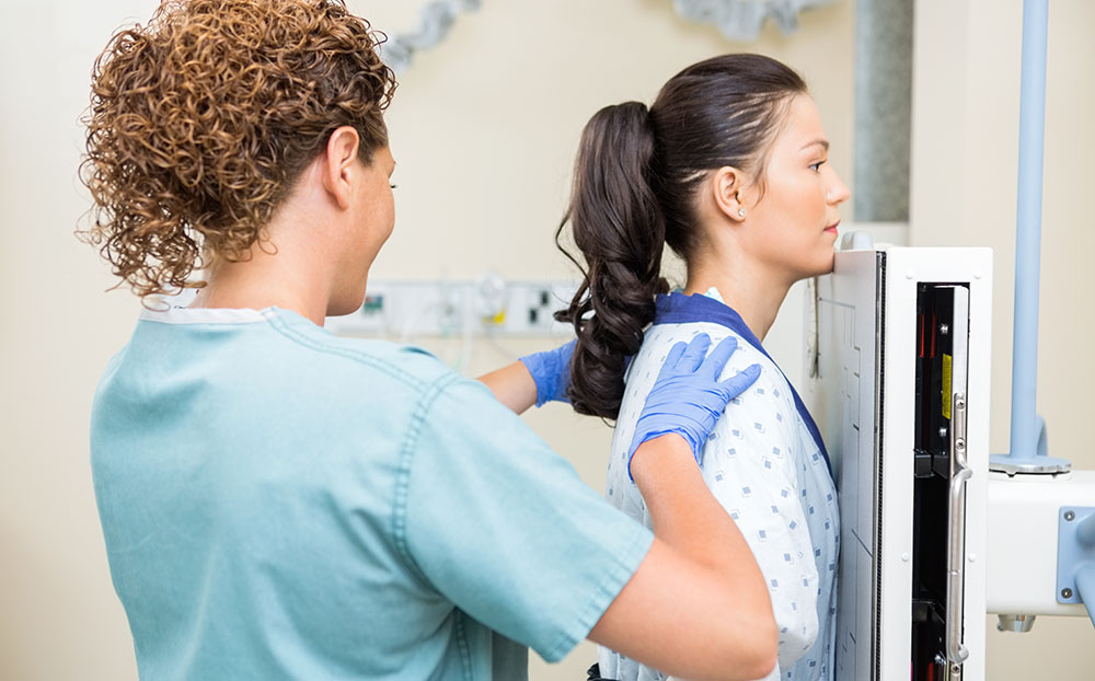 Rear view of female x-ray tech preparing patient for chest xray in examination room