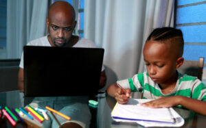 Father working on his laptop while his son draws on paper next to him