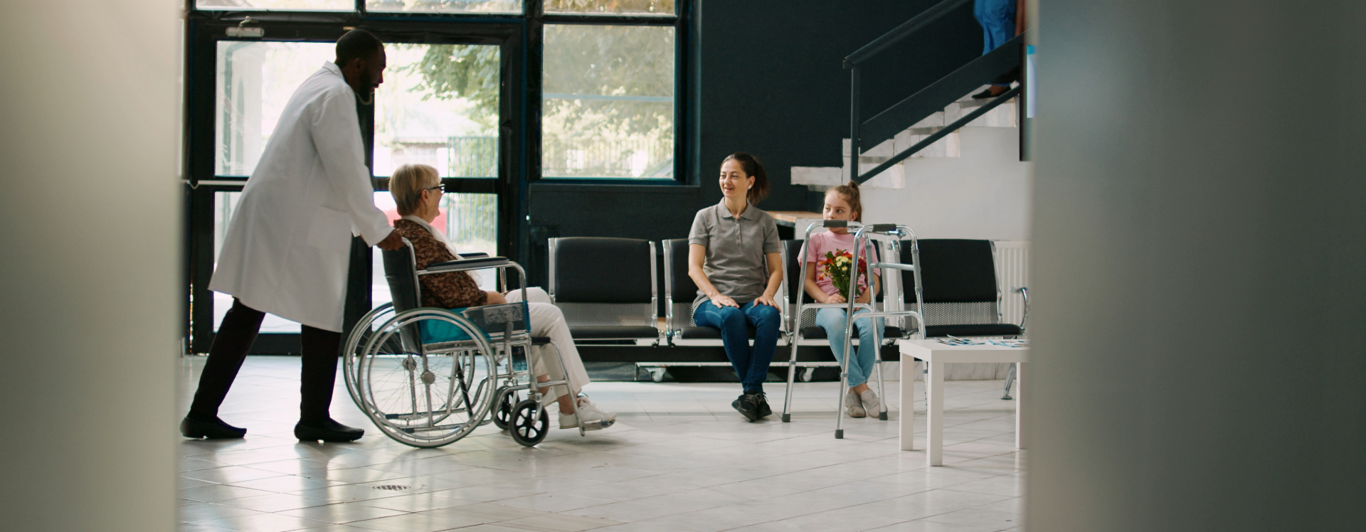 A doctor pushes a patient in a wheelchair through a hospital lobby