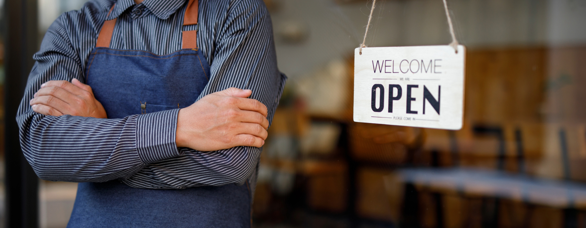person wearing a smock in front of a "we're open" business sign