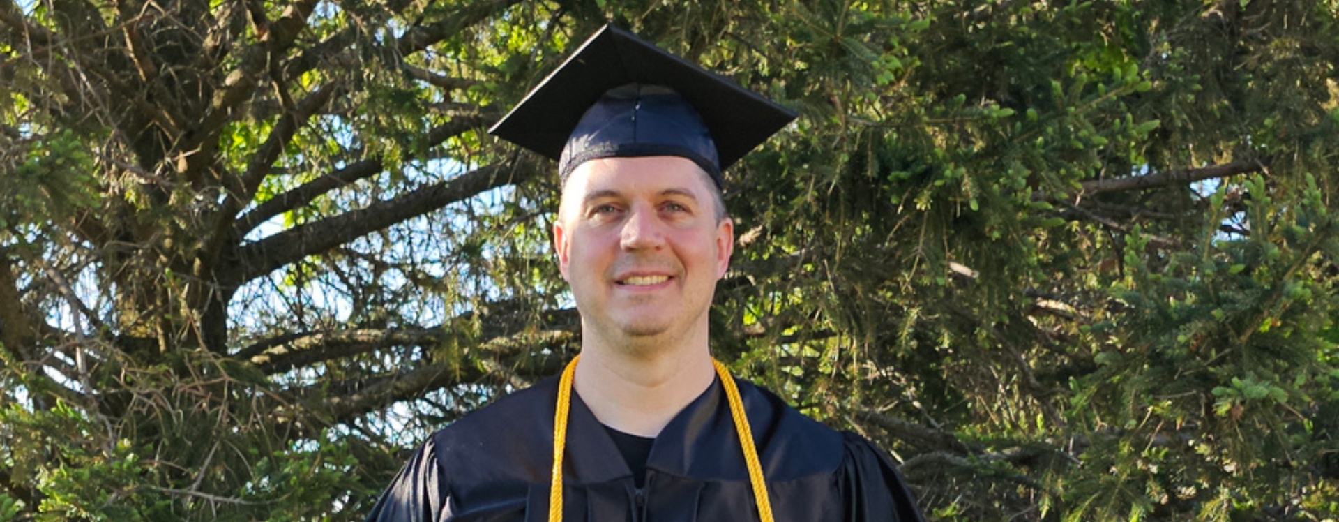 Mark Kramer wears his cap and gown while holding his diploma. Mark earned the UW Flexible Option IST degree.