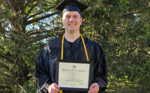 Mark Kramer wears his cap and gown while holding his diploma. Mark earned the UW Flexible Option IST degree.