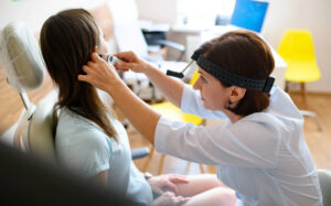 A nurse checks a patient's ear with an otoscope.