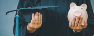 person holding a graduation cap and a piggybank