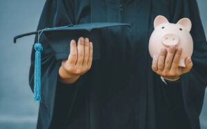 person holding a graduation cap and a piggy bank