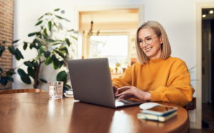 A woman smiles while using a laptop in her living room